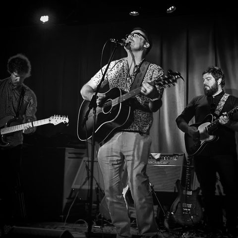 The band performing live on stage in black and white