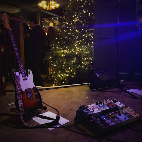 A Telecaster on its stand beside a pedalboard before a gig